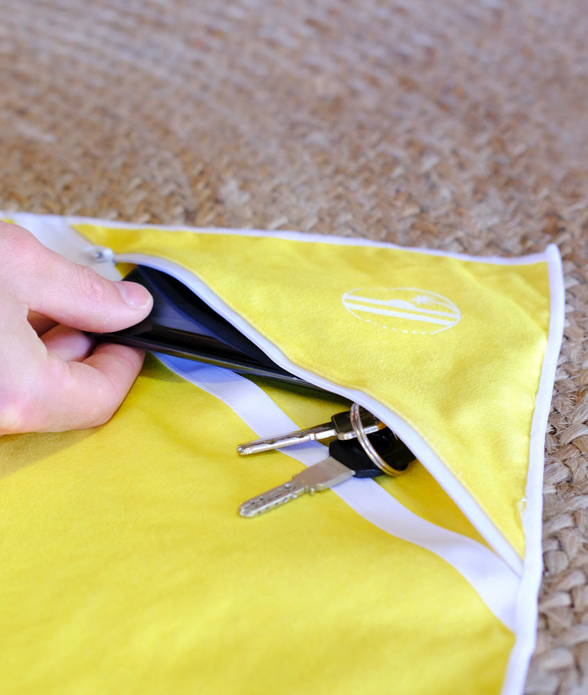 personne qui range son smartphone et ses clés dans une serviette en microfibre beachee
