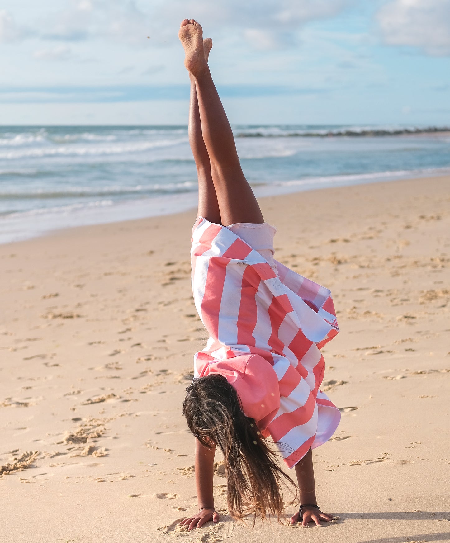 enfant faisant un poirier sur la plage habillé en poncho en microfibre