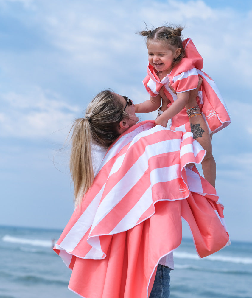 Mère qui porte sa fille devant la mer portant le même poncho de plage
