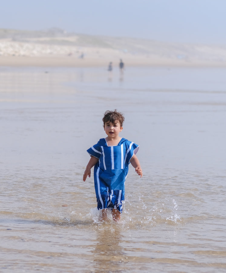 enfant avec les pieds dans la mer portant un poncho de plage bleu
