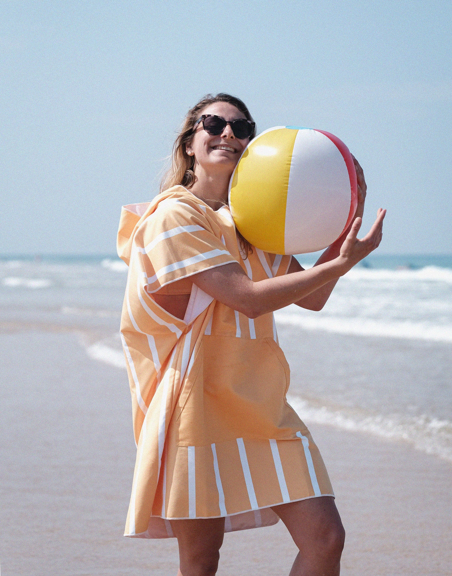 fille avec un ballon sur la plage avec un poncho rayée en microfibre orange et blanc