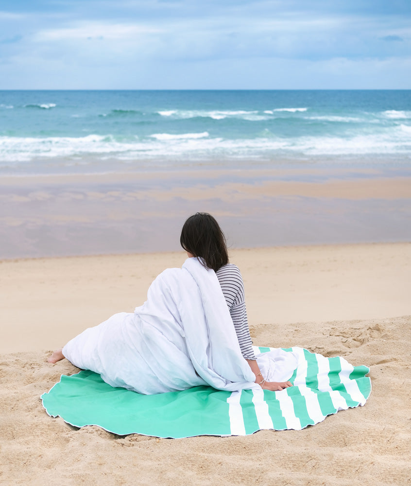 femme assise sur la plage en face de la mer sur une serviette ronde en microfibre 