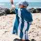jeune enfant qui fait un signe de la main en regardant la mer et qui porte un poncho en microfibre