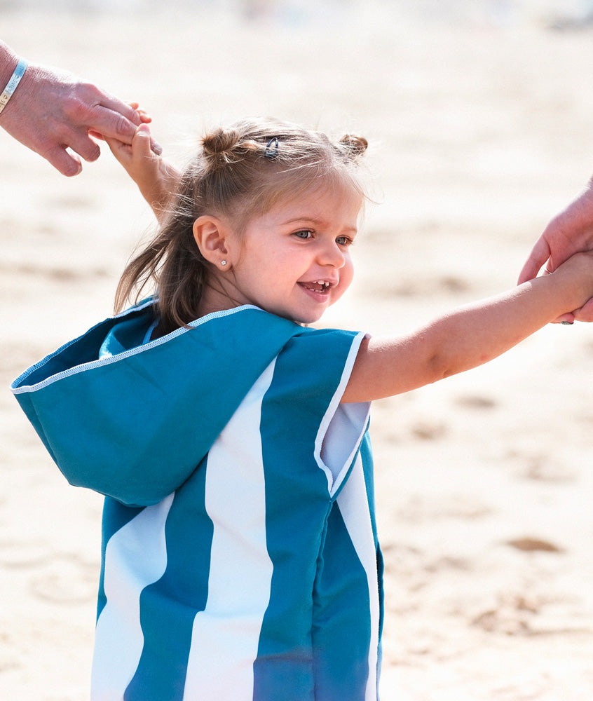petite fille qui tient la main de ses parents en marchant sur la plage habillée avec un poncho en microfibre bleu beachee