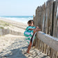 un enfant tente de grimper sur une barrière de bois avec son poncho de plage en microfibre