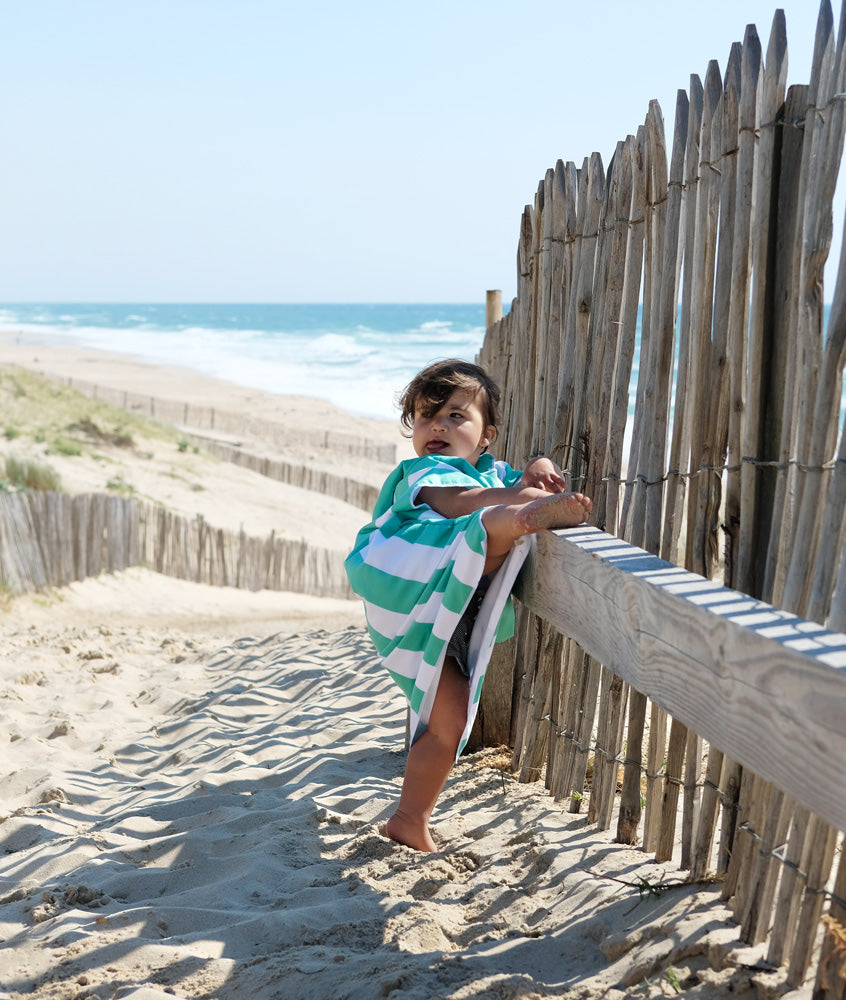 un enfant tente de grimper sur une barrière de bois avec son poncho de plage en microfibre