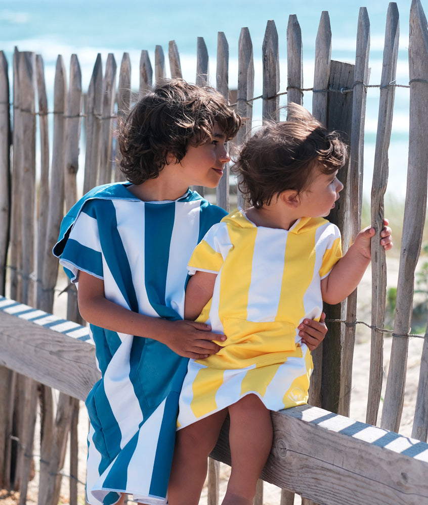 deux enfants assis sur une planche de bois qui regarde la mer vêtus d'un poncho de plage en microfibre 