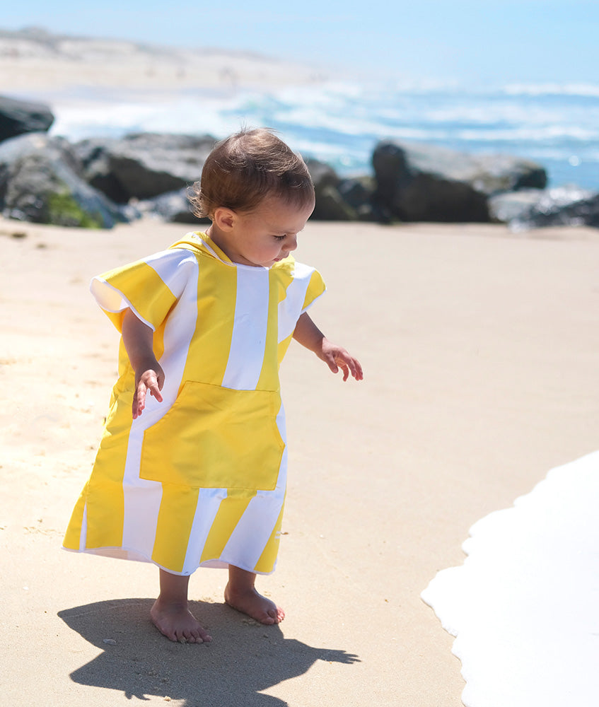 enfant en poncho jaune qui regarde l'eau de la mer