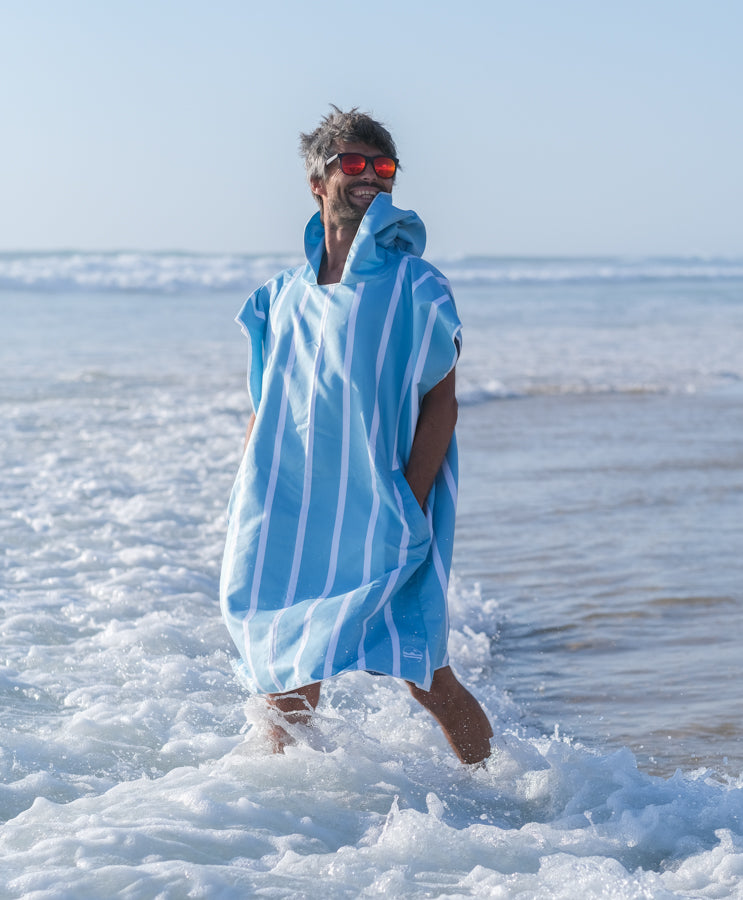 homme qui sourit et qui porte un poncho de plage bleu ciel