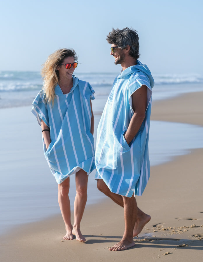 couple sur la plage qui rit portant un poncho de plage bleu ciel