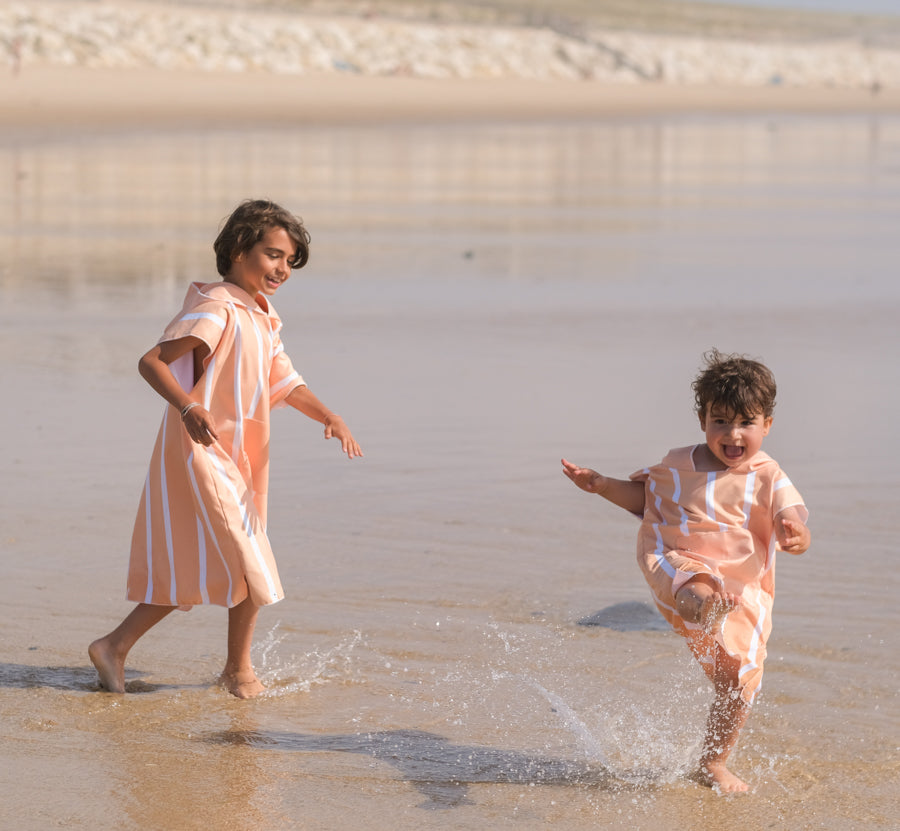 deux enfants qui courent dans l'eau avec leur poncho à rayure orange