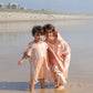 deux enfants avec les pieds dans l'eau en poncho couleur pêche 
