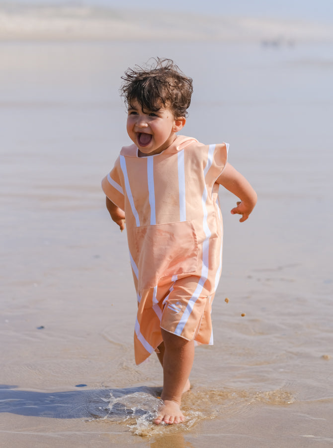 enfant qui rigole et qui marche sur la plage en poncho