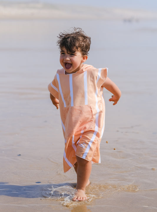 enfant qui rigole et qui marche sur la plage en poncho