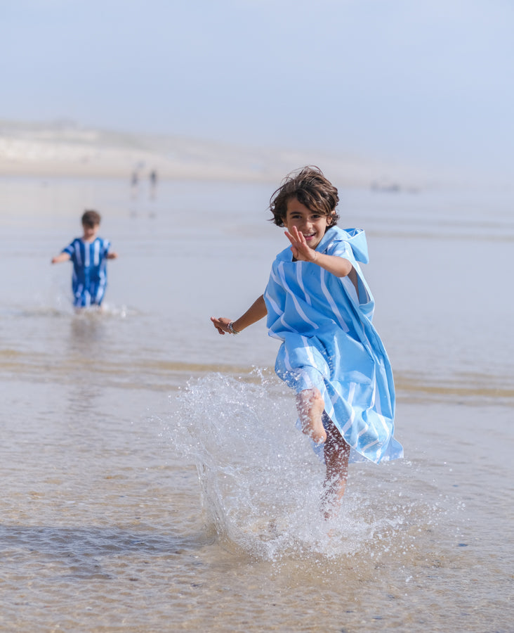 deux enfants qui courent dans l'océan avec des ponchos beachee