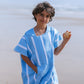 enfant qui tient un coquillage au bord de l'océan habillé en poncho bleu ciel