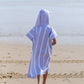 enfant de dos qui marche vers la mer et qui porte un poncho avec une capuche