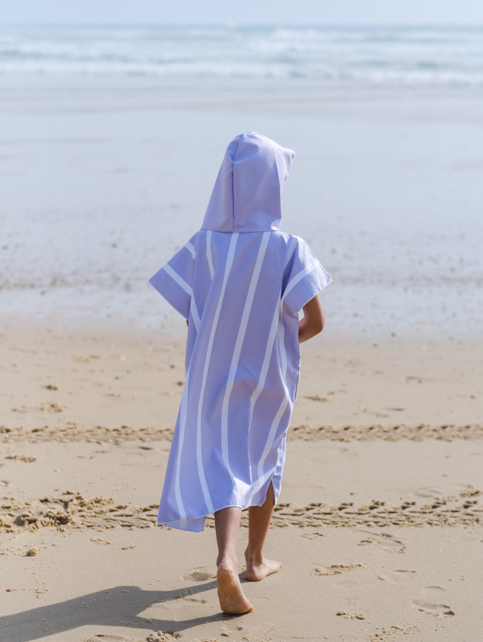 enfant de dos qui marche vers la mer et qui porte un poncho avec une capuche